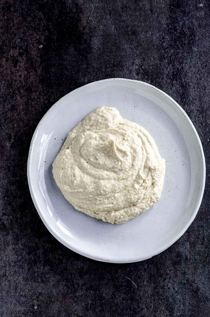 A white plate with a pile of hummus on a black surface
