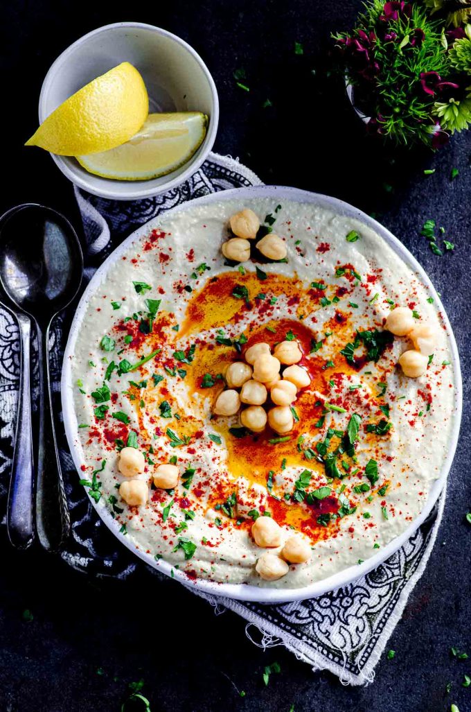 Overhead view of a plate with hummus garnished with some chickpeas, olive oil, paprika and chopped parsley