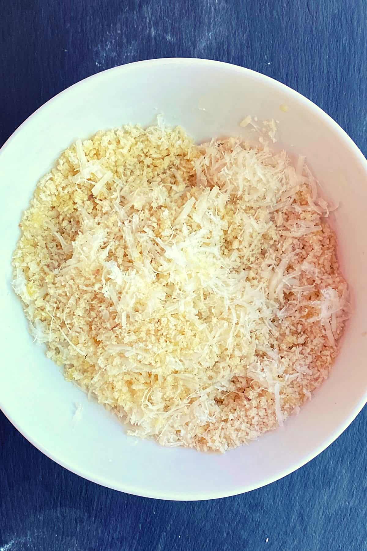 Overhead view of white bowl with shredded cheese and breadcrumb mix