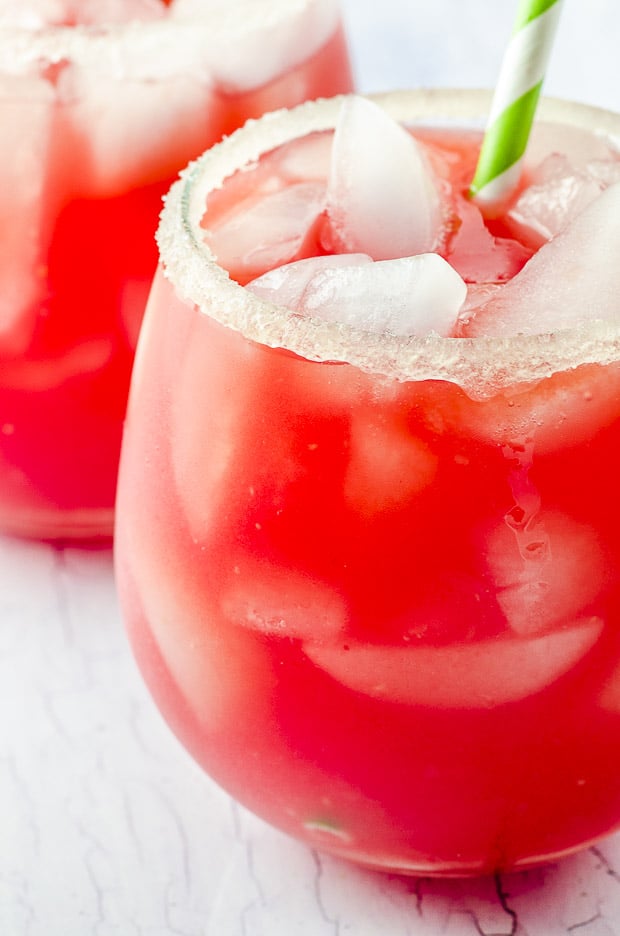 A close up view of a glass filled with ice and watermelon lemonade with a green and white straw