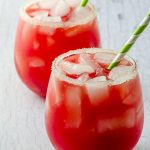 two glasses filled with watermelon lemonade and ice with a green and white paper straw