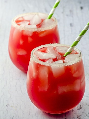two glasses filled with watermelon lemonade and ice with a green and white paper straw