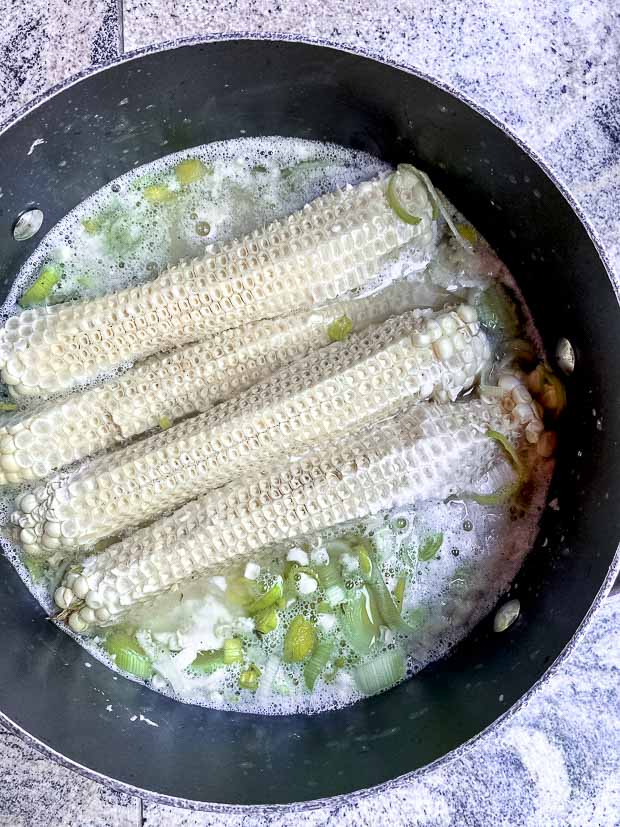 Corn soup cooking a pot. Water, leeks, potatoes, and corn cobs.