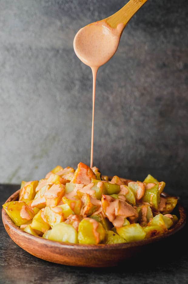 verter salsa bravas en un plato de patatas para hacer de las patatas bravas una tapa tradicional de España. Una de nuestras recetas vegetarianas de Pascua.