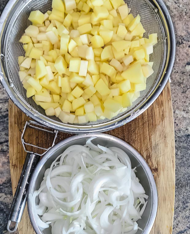 Bird's eye view of two bowls, one with cut potatoes and another one with onions