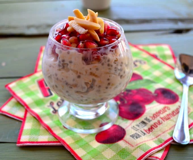 A glass cup with overnight oats topped with pomegranates and almonds