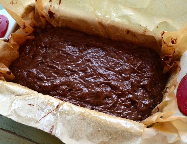 Loaf pan lined with parchment paper with vegan chocolate cake batter in it, before going in the oven