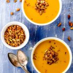 Bird's eye view of two white bowls filled with vegan pumpkin soup and topped with savory granola