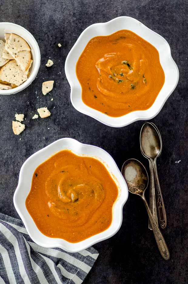 Bird's eye view of two white bowls filled with tomato and roasted eggplant soup on a black surface. One of our vegetarian Passover recipes.
