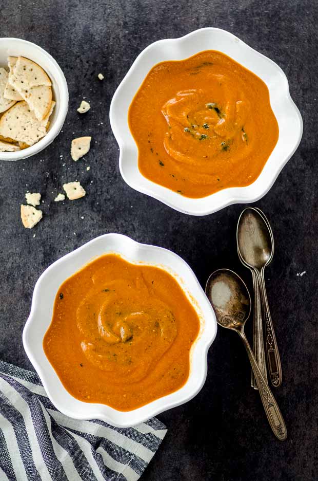 Vista a volo d'uccello di due ciotole bianche ripiene di pomodoro e zuppa di melanzane arrostite su una superficie nera. Una delle nostre ricette pasquali vegetariane.