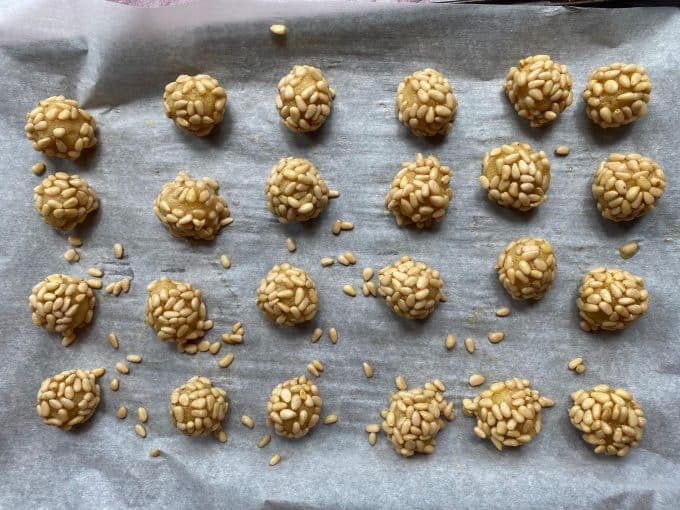 an overhead view of a parchment paper lined cookie sheet with cookie dough balls with pine nuts on them