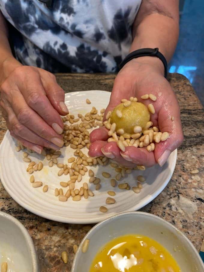 a view of hands placing pine nuts onto pignoli cookie dough balls