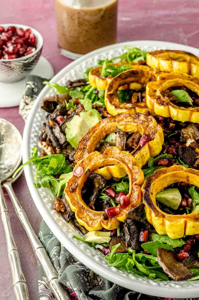 Close up side view of a platter with arugula salad topped with roasted delicata squash, and pomegranates