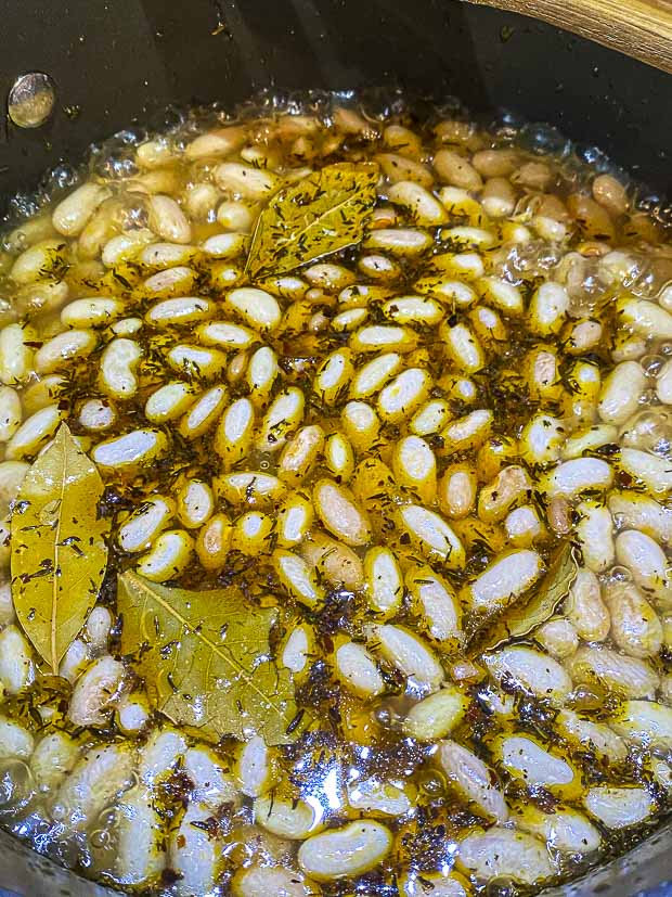 Cranberry beans cooking in a pot with water herbs and bay leaves