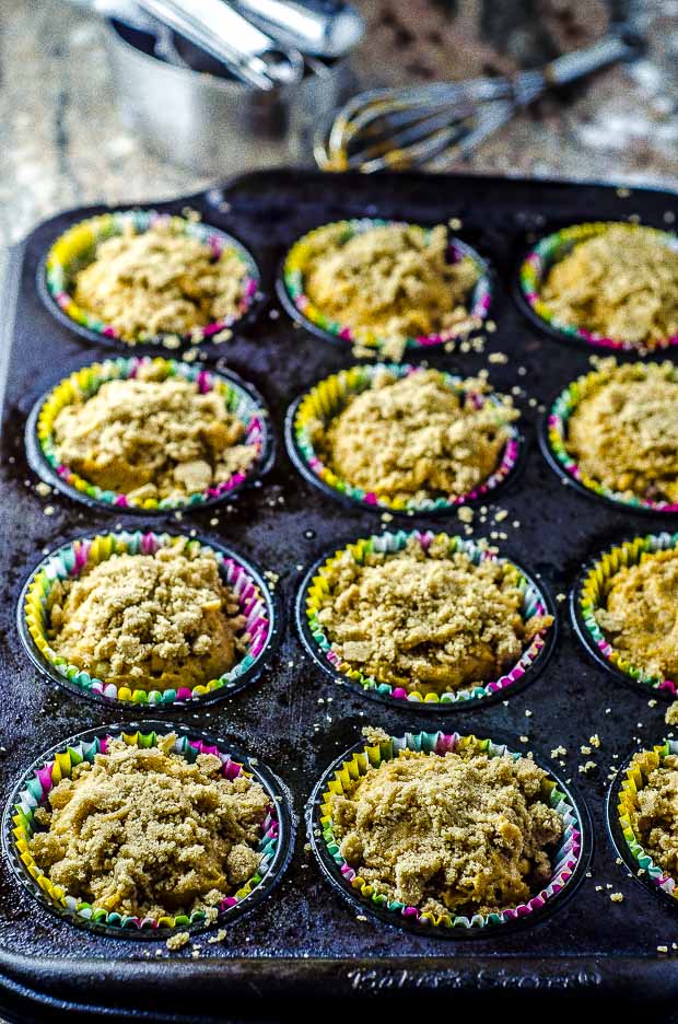 Vegan pumpkin muffin batter top with a streusel in a muffin tin lined with multicolor muffin tin liners.