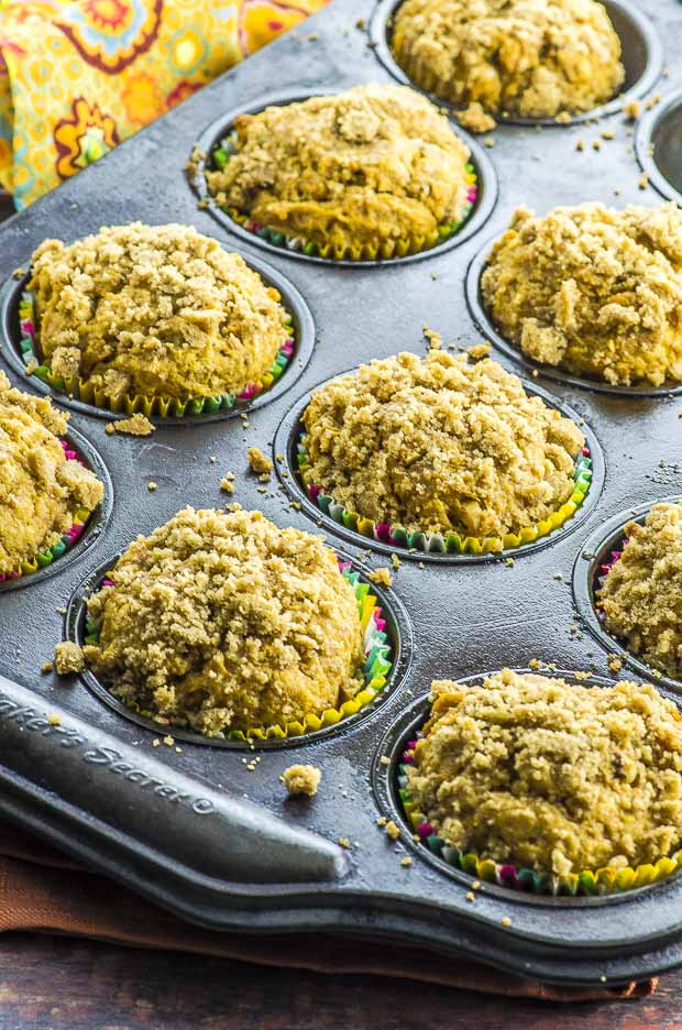 Baked Vegan pumpkin muffin topped with a streusel in a muffin tin lined with multicolor muffin tin liners.