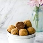 Side view of two staked bowls filled with dark chocolate truffles with a vase with flower in the background