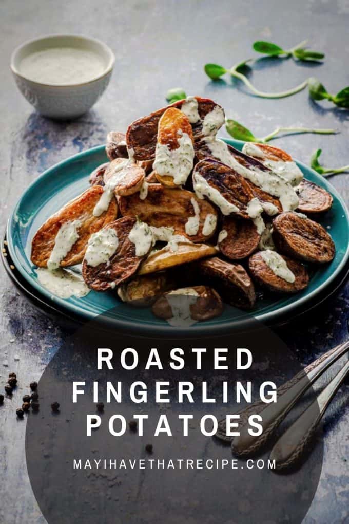 A tilted view of a bowl of roasted fingerling potatoes with horseradish sauce drizzled on top