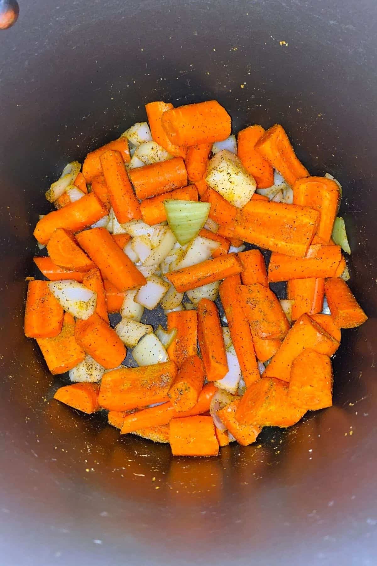 An overhead view of a pot with sliced carrots and onions with seasonings and vegetable broth poured over