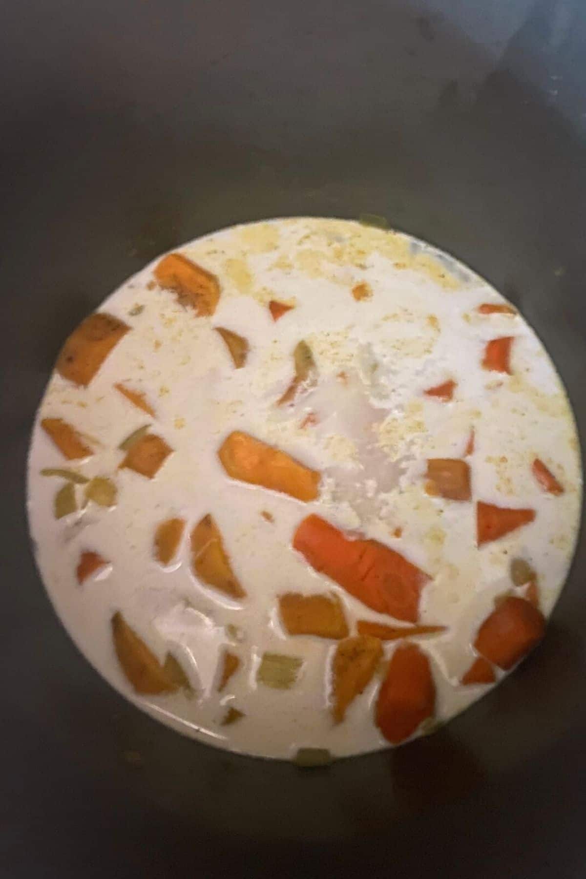 An overhead view of a pot of creamy carrot soup ingredients with coconut milk poured over