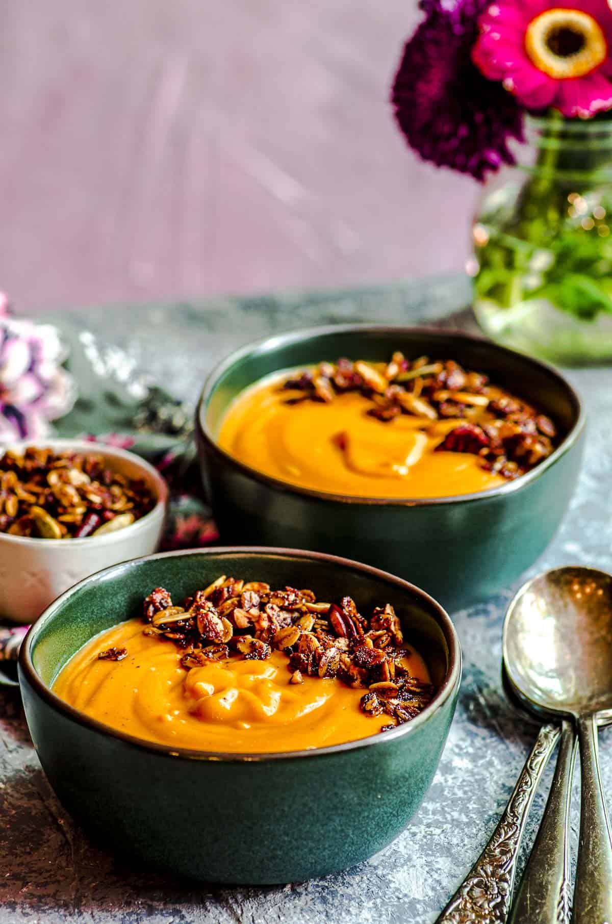 A tilted view of two blue bowls of carrot soup