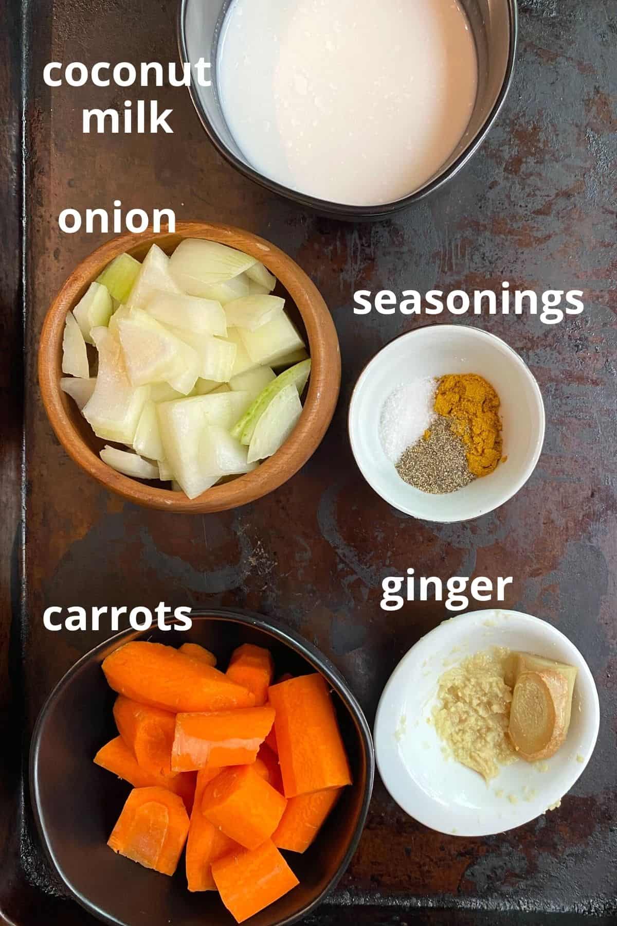 An overhead view of the ingredients to make creamy carrot soup; coconut milk, onion, seasonings, carrots, ginger