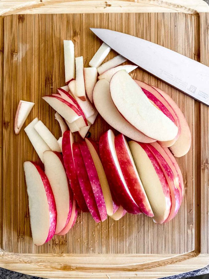 Sliced apples on a wood cutting board to make kohlrabi slaw