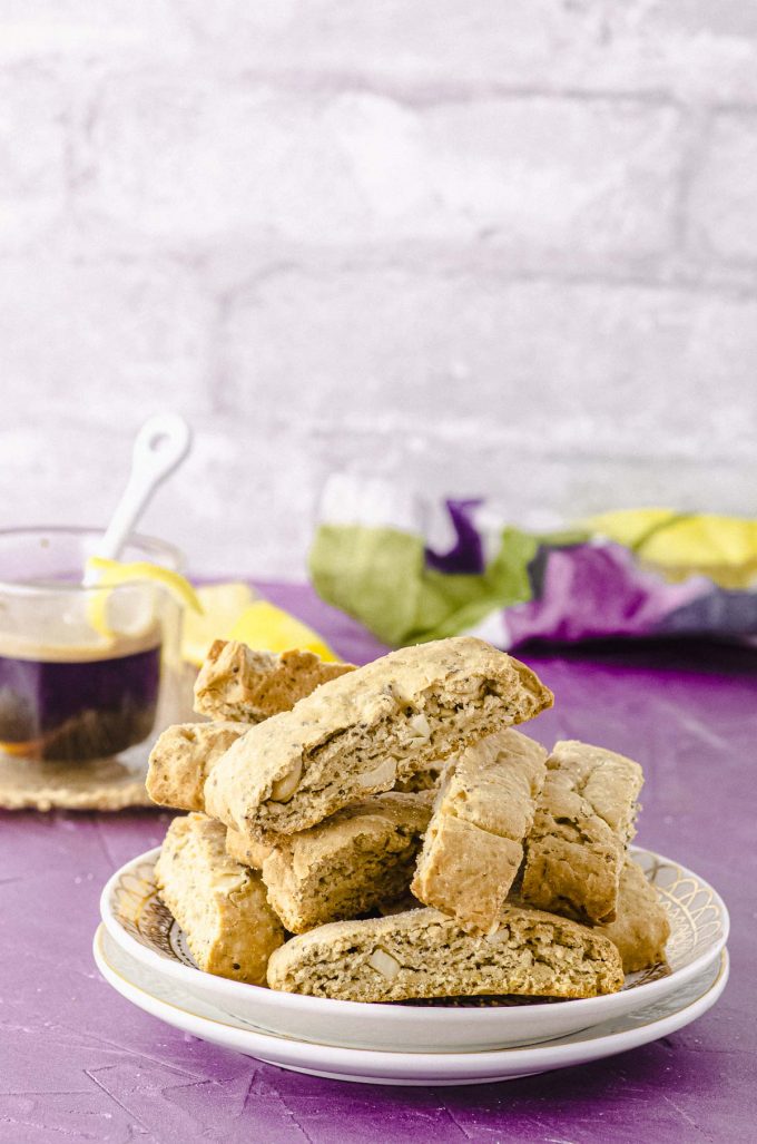 A pile of biscotti on a plate with a coffee in the background