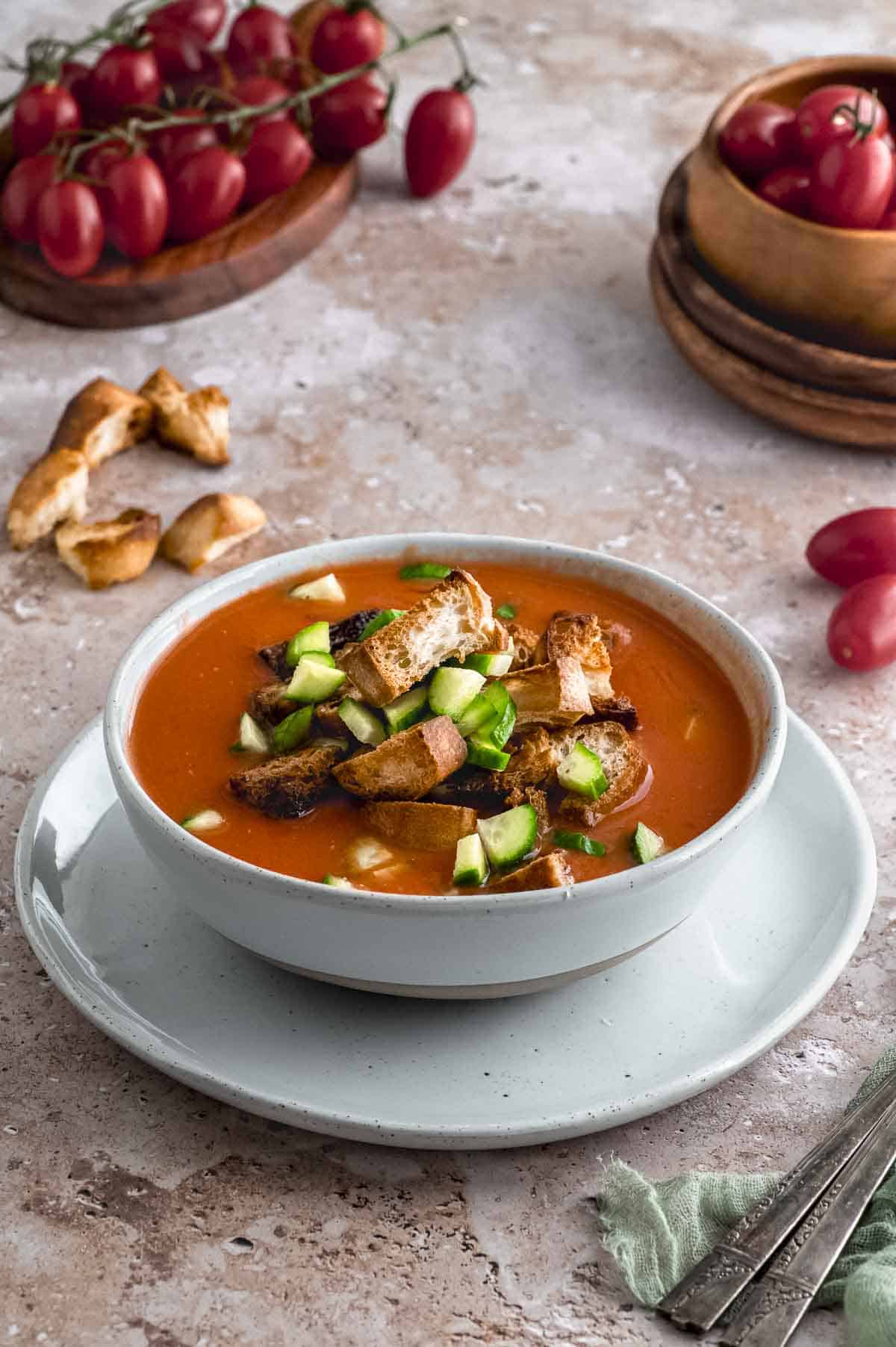 Side view of a bowl of gazpacho topped with croutons and cucumbers
