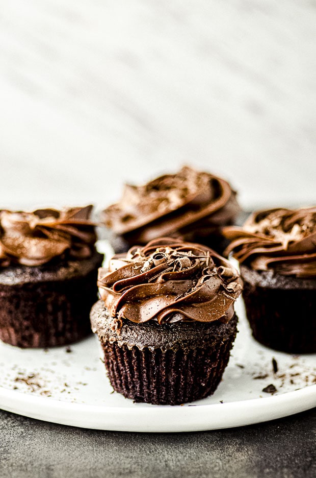 Side view of four chocolate cupcakes with chocolate frosting on a white plate