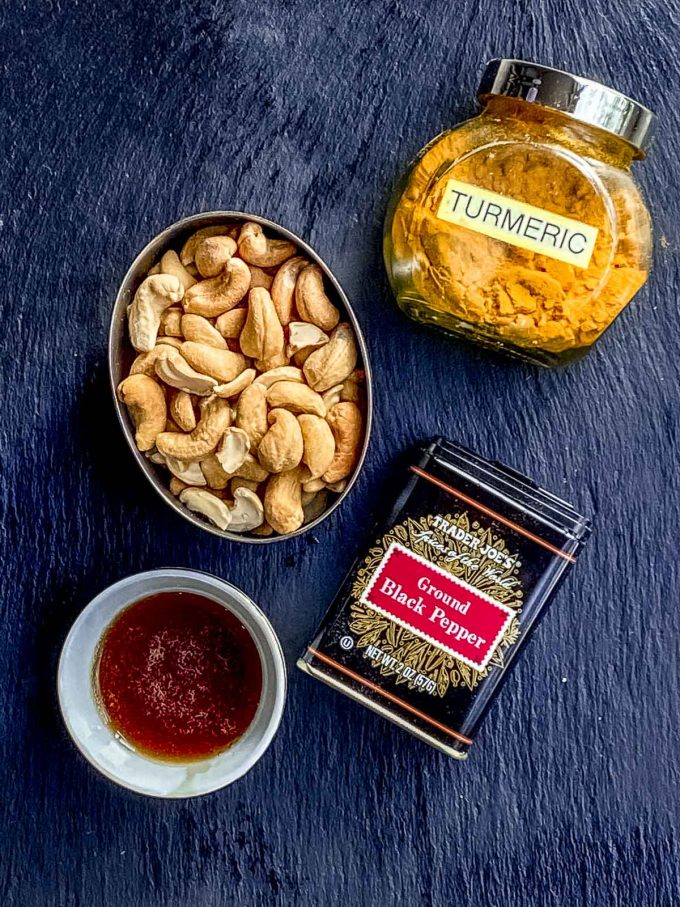 Ingredients to make spiced cashews: roasted cashews, turmeric, black pepper and maple syrup
