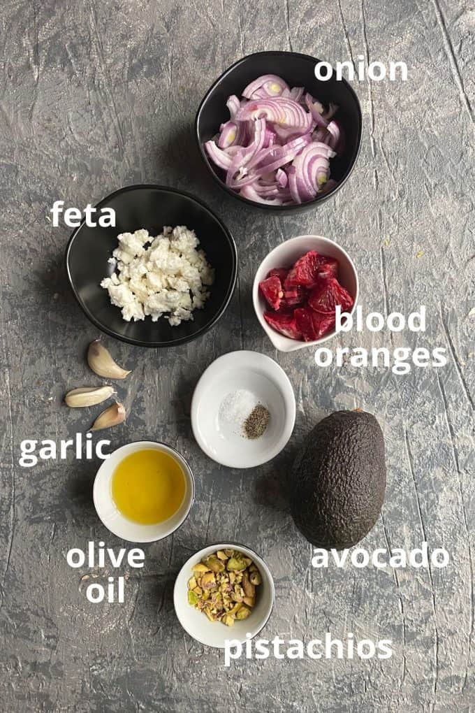 The ingredients to make blood orange salad; red onions, feta, blood oranges, garlic, olive oil, avocado, pistachios