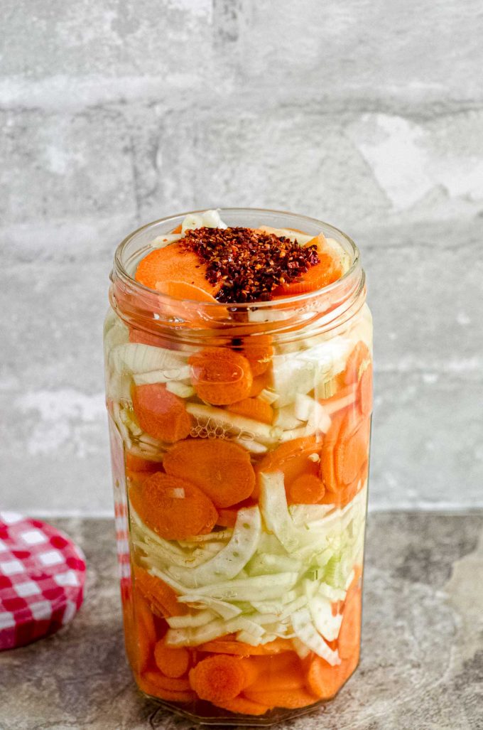 Hot pepper flakes on top of jar of pickled carrots and fennel