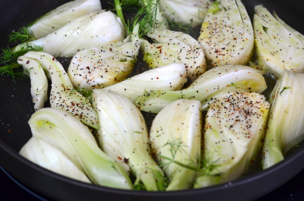Close up of raw fennel quarters sprinkled with black pepper in a skillet