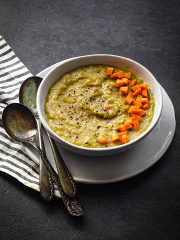 45 degree angle photo of a white bowl with split pea soup with carrots on top