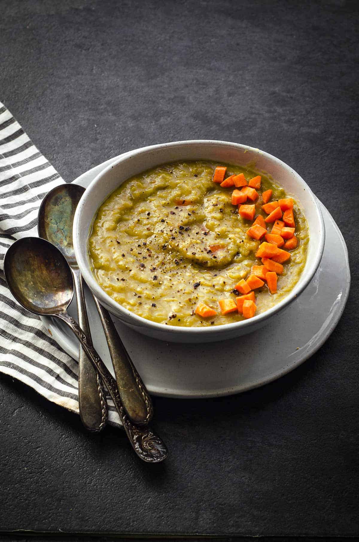 45 degree angle photo of a white bowl with split pea soup with carrots on top