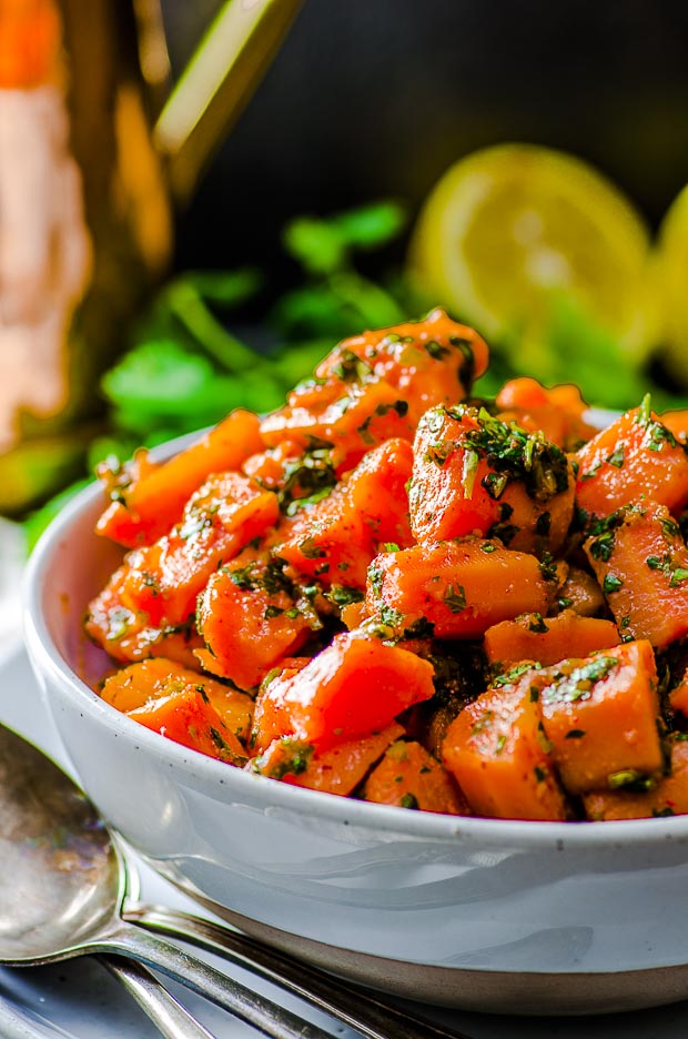 A Close Up of a A Bowl of moroccan carrot salad with a lemon cut in half on the background