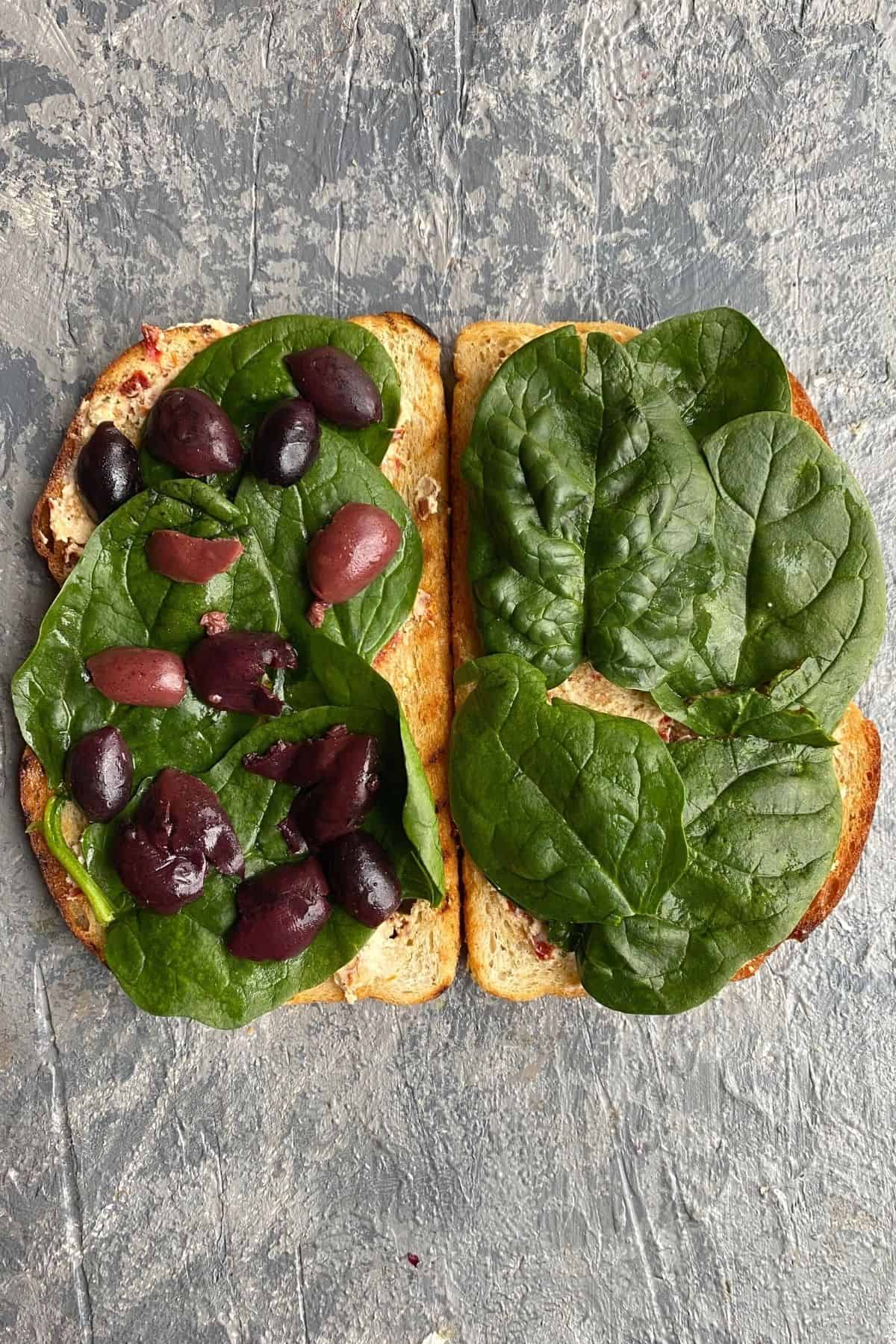 Two pieces of bread with spinach and olives