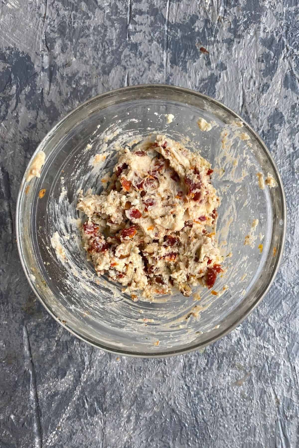 A mixture of garlic cheese, sun dried tomatoes and walnuts in a mixing bowl