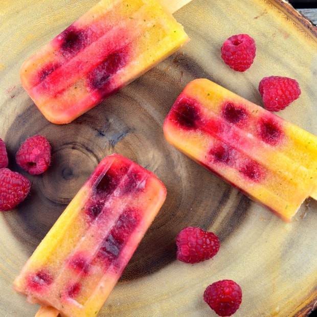 birds eye view of three Cucumber-Melon-Lemon Popsicles on a round wood board with some raspberries scared around