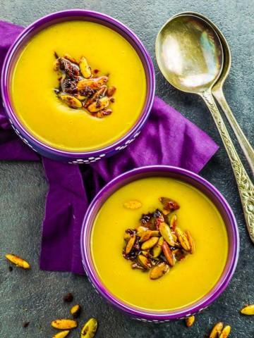 Bird's eye view of two purple bowls filled with butternut squash soup and topped with roasted pumpkin seeds
