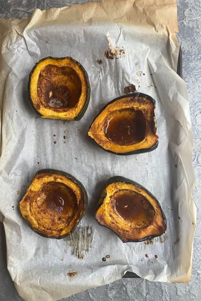 An overhead view of baked acorn squash halves on a parchment paper lined baking sheet