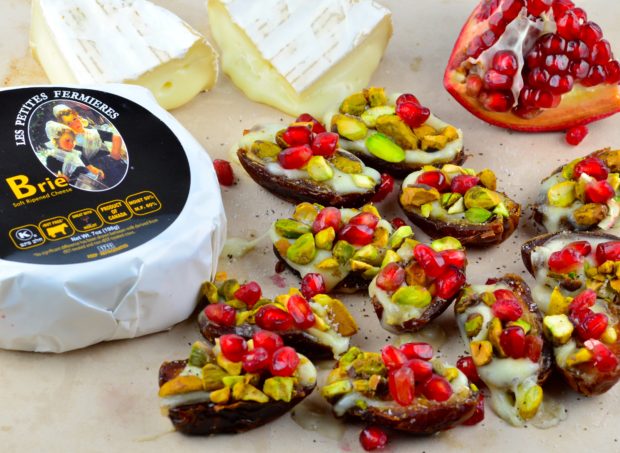 Several medjoop dates cut in half and filled with warm brie with a wheel of brie and a piece of pomegranate fruit in the background