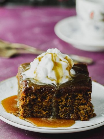 A close up on a vegan sticky toffee pudding topped with whipped cream