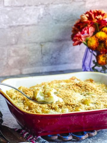 A tilted view of a red baking dish with cauliflower gratin