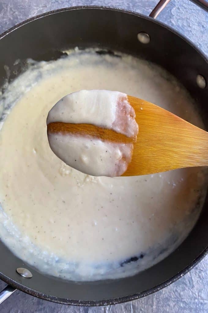 An overhead view of bechamel sauce with a wooden spoon hovering over