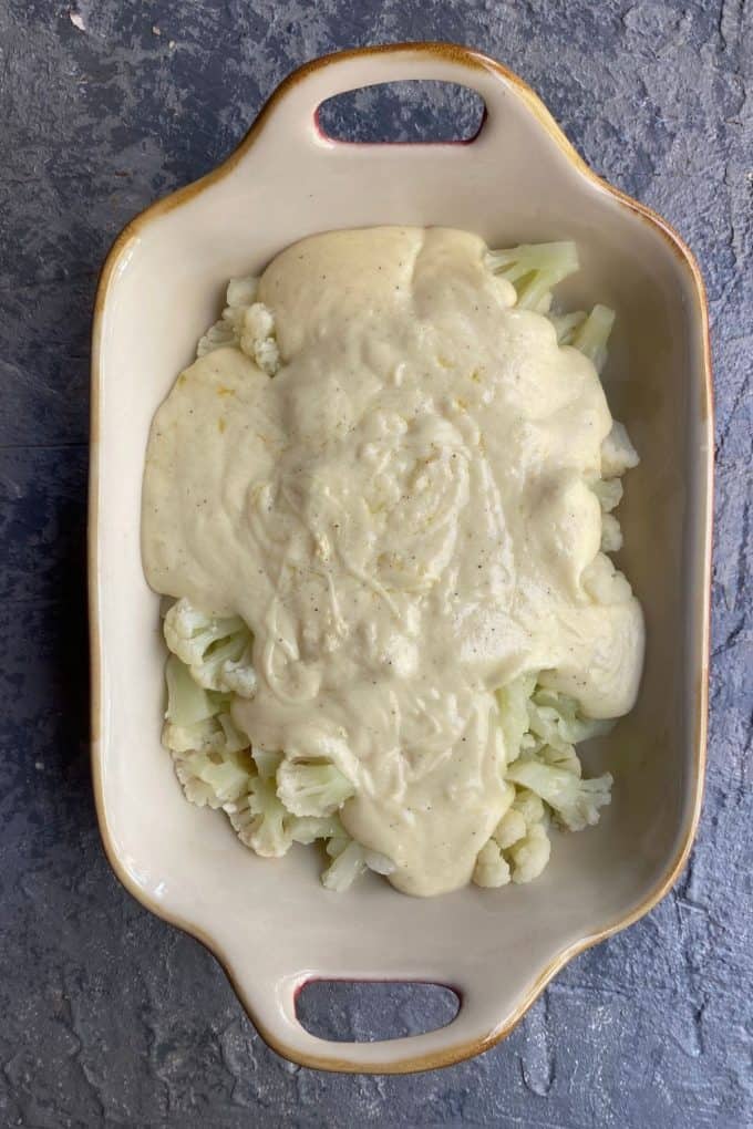 An overhead view of a baking dish with bite sized cauliflower covered in bechamel sauce