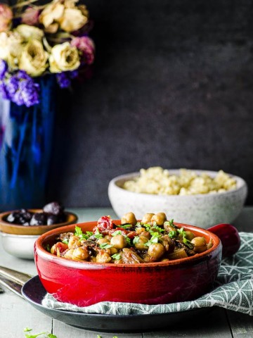 Side view of a red stone wear bowl with fennel and chickpea stew with a bowl of quinoa in the background