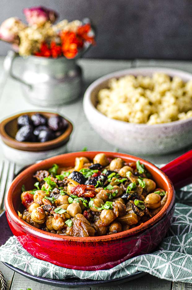 Forty five degree view of a red stone wear bowl with fennel and chickpea stew with a bowl of quinoa in the background