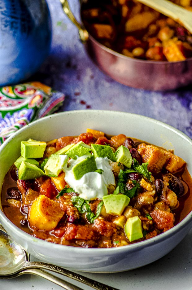 Close up view of a white bowl filled with sweet potato chili topped with fresh avocado cubes